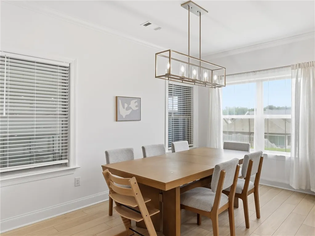 Natural light floods this dining area, featuring blonde hardwood flooring and a linear chandelier.