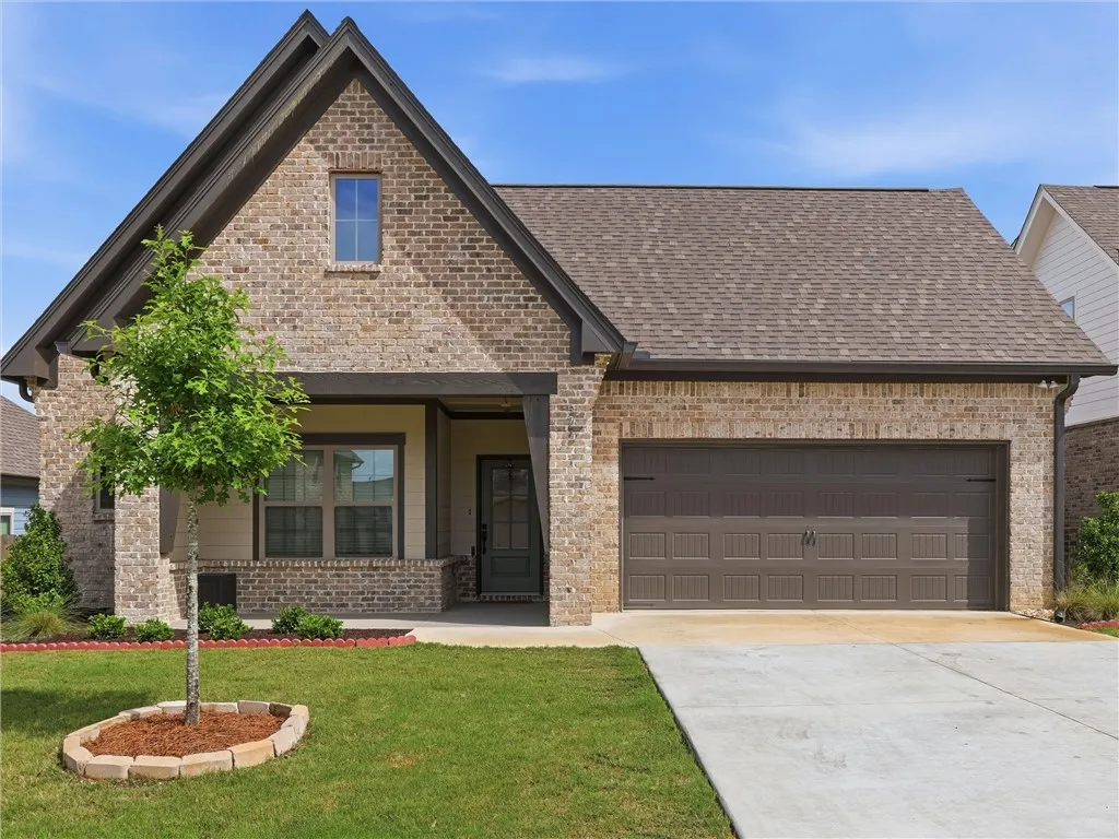 A charming brick residence showcases a convenient attached garage and a neatly maintained front lawn.