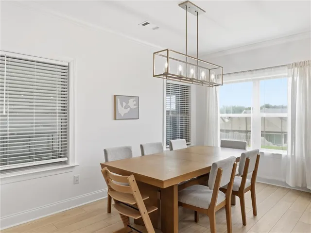 Natural light floods this dining area, featuring blonde hardwood flooring and a linear chandelier.