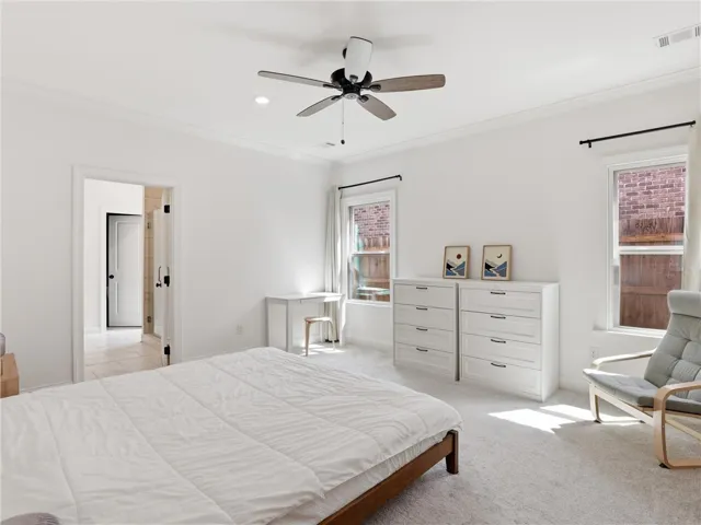 A well-lit bedroom features a ceiling fan, plush carpet, and dual windows allowing natural light to fill the space.