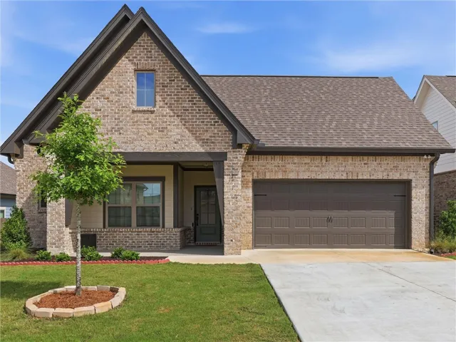 A charming brick residence showcases a convenient attached garage and a neatly maintained front lawn.