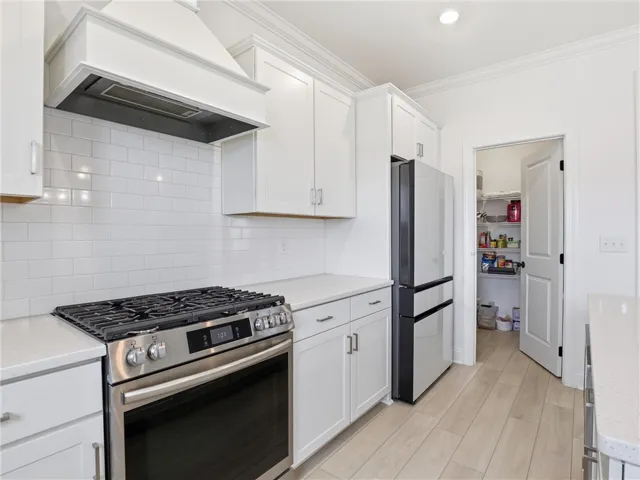 White cabinetry and subway tile backsplash frame a sleek gas range, complemented by modern appliances and a convenient walk-in pantry.