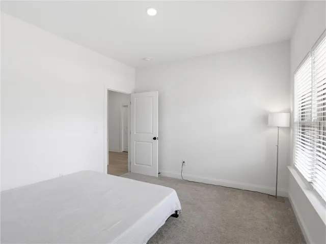 Recessed lighting illuminates this inviting bedroom, featuring plush carpet and a clear view of the outdoors.