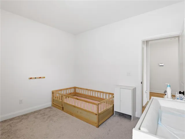 A well-lit nursery features soft carpeting and a clear doorway leading to an adjoining space.