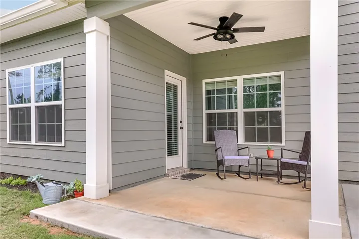 A spacious concrete patio invites outdoor relaxation with rocking chairs and a refreshing ceiling fan.