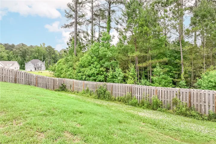 A verdant backyard with a wooden fence borders a dense woodland, offering privacy and natural beauty.