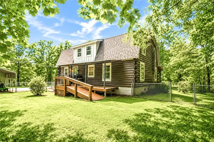 A charming log home with a gabled roof and accessible wooden deck is nestled among verdant trees.