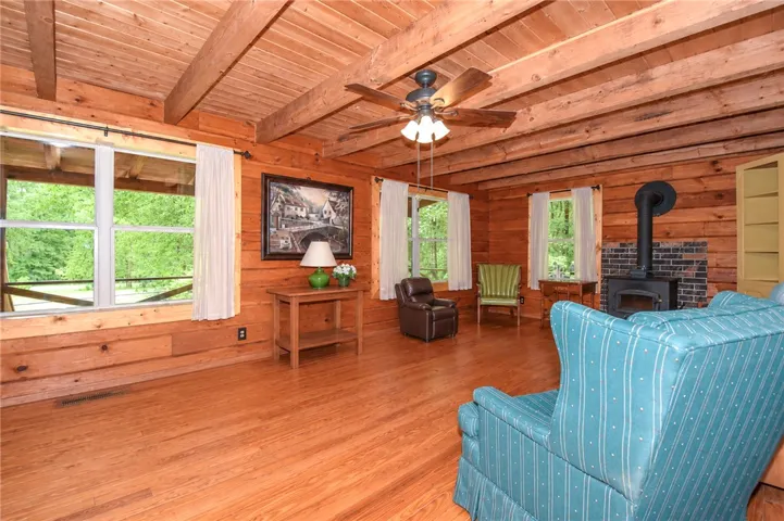 A rustic living space with wooden walls and ceiling beams, featuring a cozy fireplace.