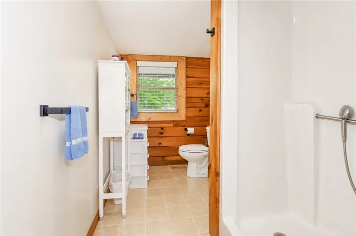 A well-lit bath with warm wood paneling, featuring a window and a practical shower stall.