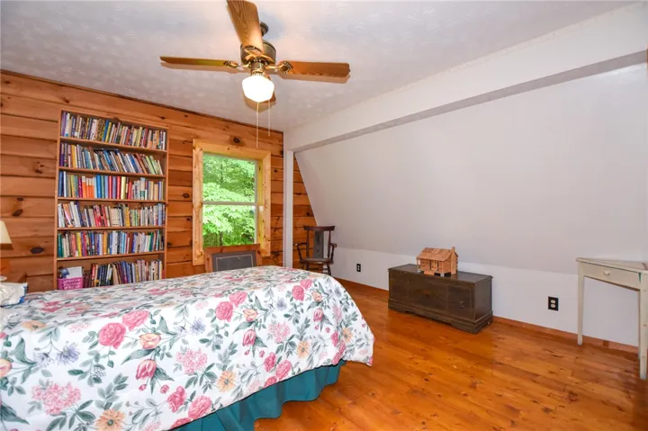 A cozy bedroom with a built-in bookcase and wood paneling offers a serene, wooded view.