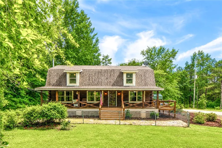 A charming log cabin-style home with a spacious front porch, nestled among vibrant greenery.