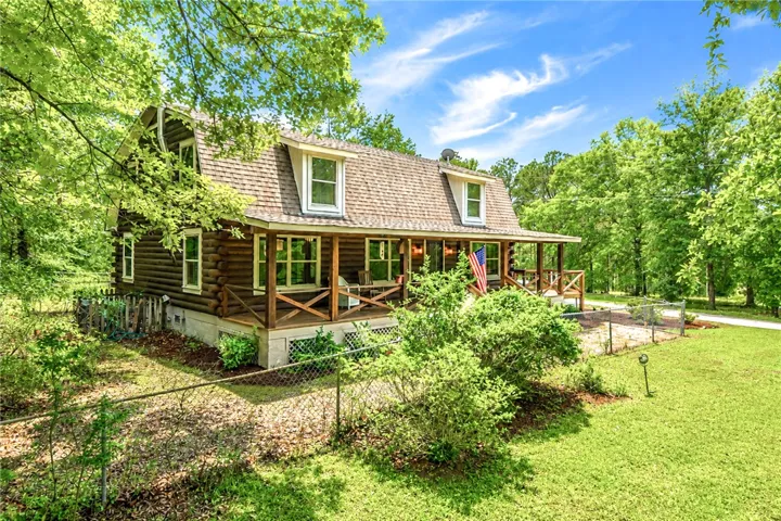 A classic log cabin style home, nestled amongst lush trees, boasts a charming front porch.
