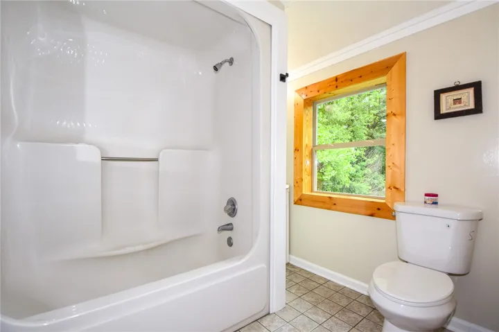 A well-maintained bathroom with a combination shower and tub, offering natural light through a wooden-framed window.