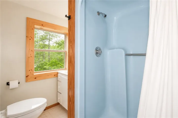 A window in the bathroom allows natural light and tree views, complementing the shower area.