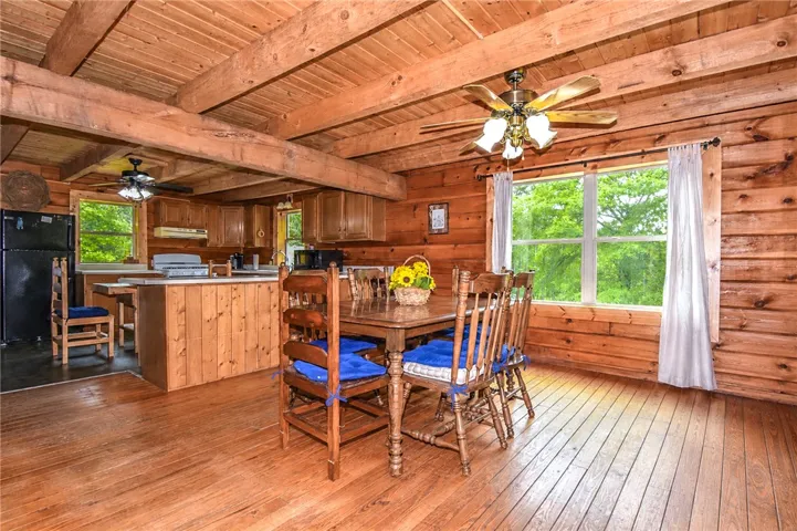 A rustic cabin kitchen and dining area features natural wood floors and large windows framing verdant outdoor views.