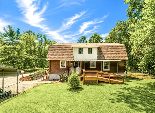 A charming log cabin-style home offers a spacious deck and welcoming front porch amidst a verdant landscape.