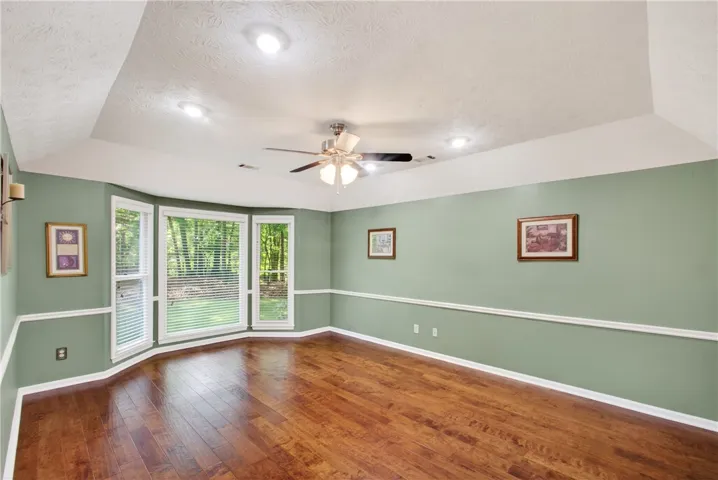Hardwood flooring extends throughout this light-filled room, featuring a tray ceiling and a ceiling fan.