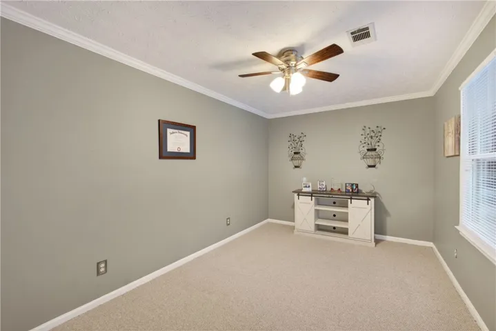 A well-proportioned room features crown molding, plush carpeting, and a ceiling fan for comfort.