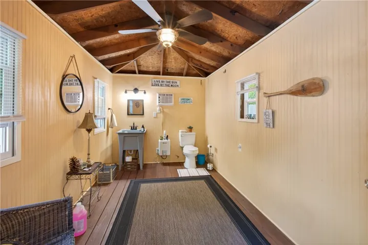 A quaint bathroom with wood paneled walls, a ceiling fan, and exposed wood beams.