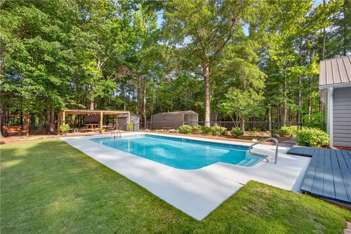 An inviting in-ground pool awaits, perfectly nestled amidst green landscaping and mature trees for ultimate privacy.