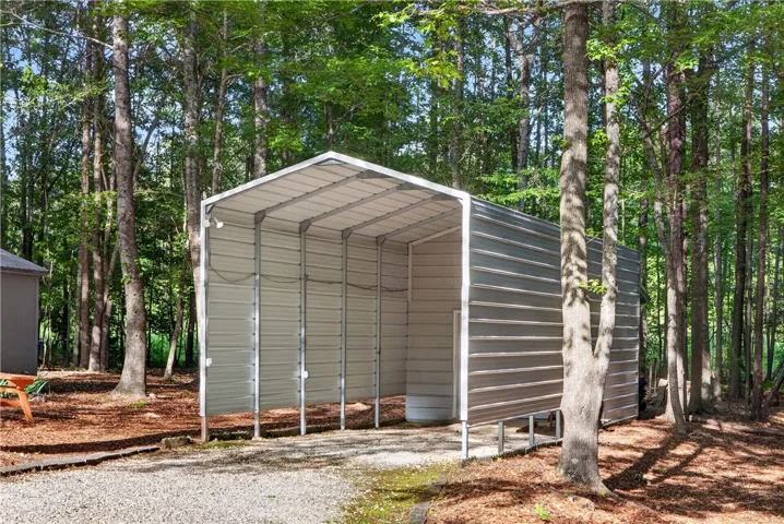 A durable carport provides shelter amidst a verdant, wooded backdrop, offering practical outdoor storage.