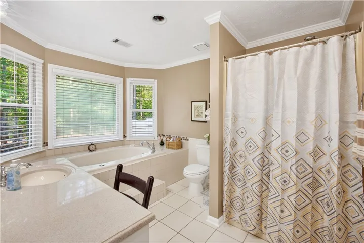 A well-lit primary bathroom featuring a large soaking tub beneath bay windows and a spacious shower.
