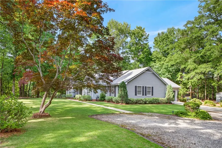 Mature trees provide a natural canopy over this inviting single-story residence with a gravel driveway.