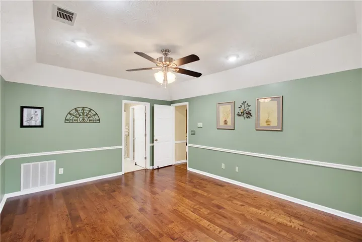 Rich hardwood flooring complements the tray ceiling and ceiling fan in this ample living space.