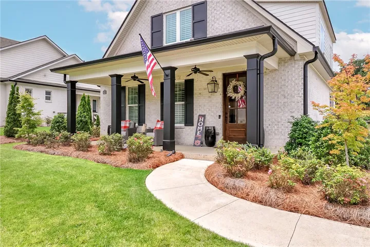 A graceful sidewalk curves toward a welcoming porch with stately columns, showcasing manicured landscaping and vibrant foliage.