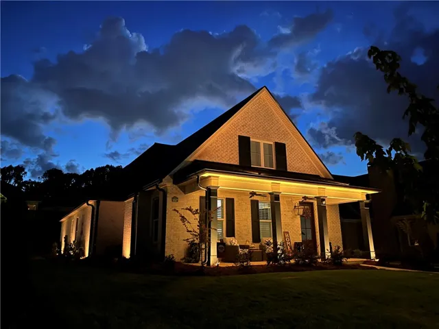 Illuminated brick facade and inviting covered porch greet guests under a twilight sky.