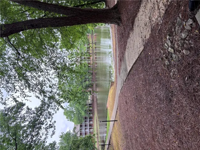 A tranquil lakeside setting with mature trees offers a serene escape, blending natural beauty with nearby structures.