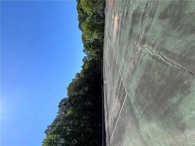 A well-maintained tennis court awaits your game, surrounded by towering, verdant trees under an azure sky.