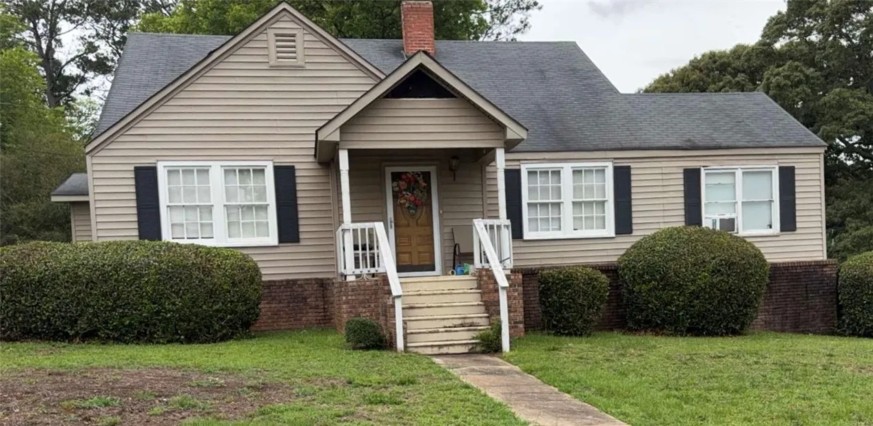 A charming cottage facade featuring a covered porch entry and well-maintained shrubbery.