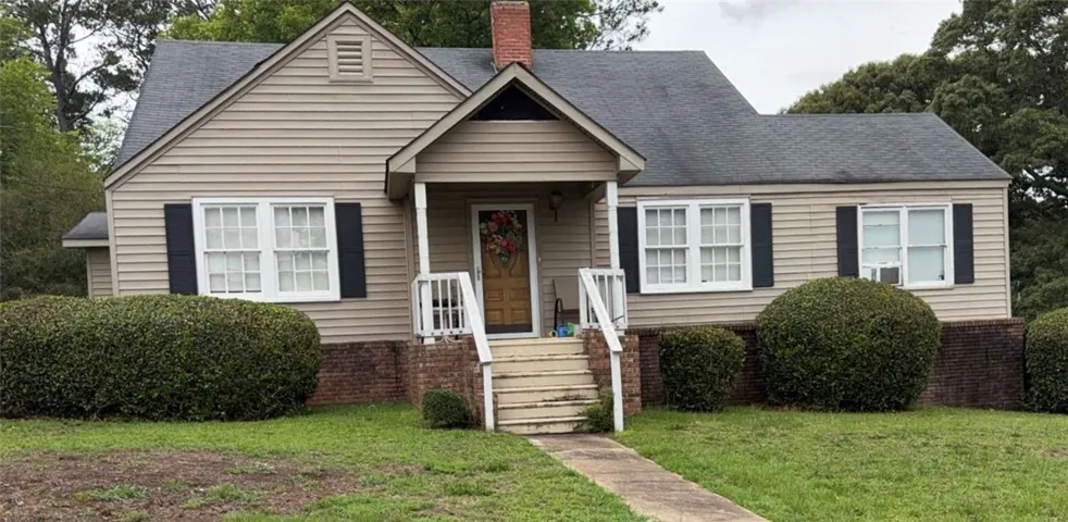 A charming cottage facade featuring a covered porch entry and well-maintained shrubbery.