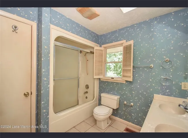 A compact bathroom featuring a shower-tub combo, a toilet, and a vanity with dual sinks.