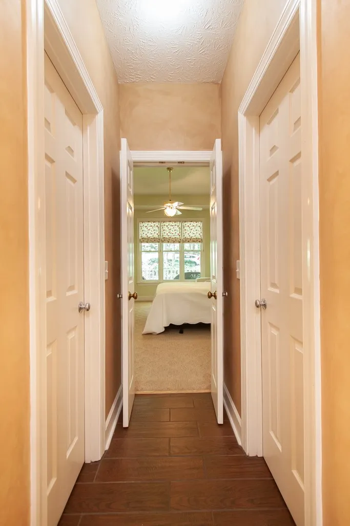 A well-lit hallway with rich wood flooring leads to a tranquil bedroom.