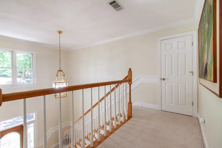 A graceful staircase with wood and white balusters leads to the upper landing, featuring a classic chandelier and natural light.