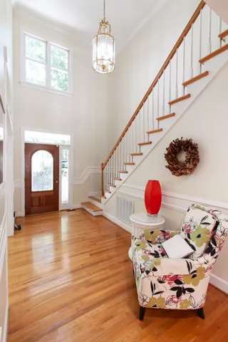 A graceful staircase ascends from a welcoming foyer featuring a polished hardwood floor and a sun-filled transom window.