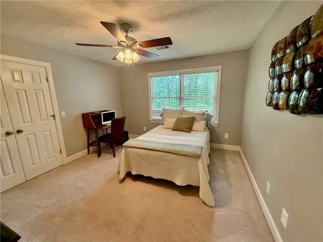 A comfortable bedroom featuring soft carpeting and a ceiling fan for year-round comfort.