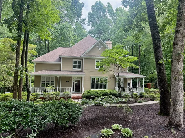 A classic home nestled amongst a verdant tree canopy, featuring a welcoming wrap-around porch.