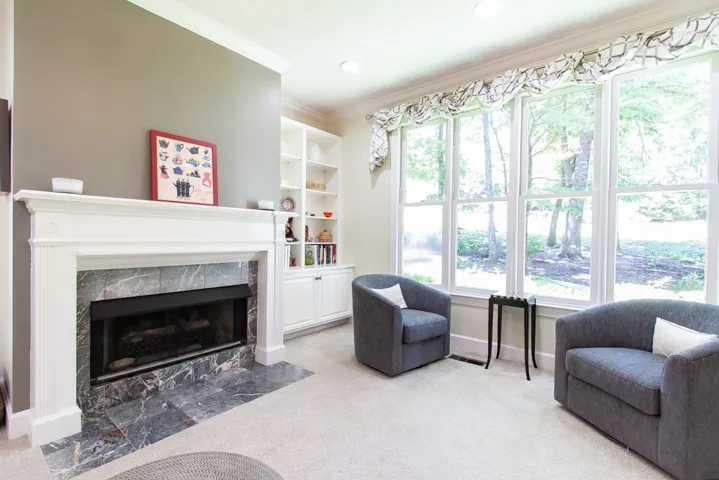 A refined living space features a marble-surrounded fireplace and abundant natural light from wide windows.