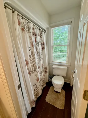 A window-lit bathroom offers a full bath with a shower and rich wood flooring.