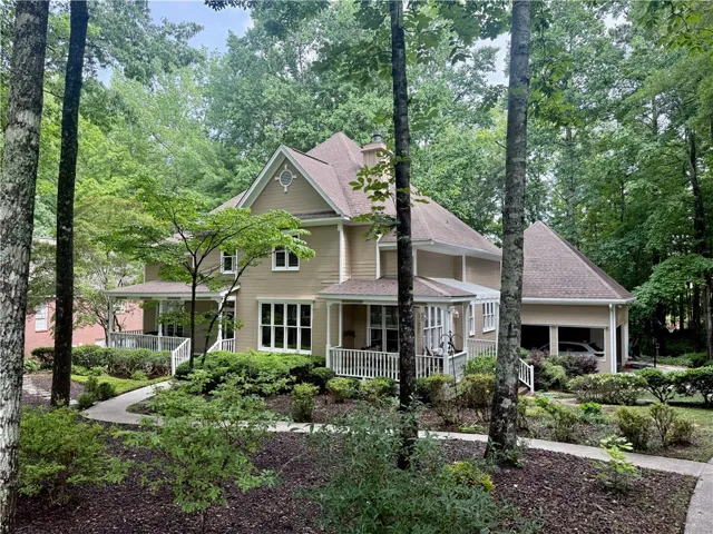 A graceful home nestled among mature trees, boasting a welcoming front porch and a paved walkway.