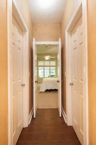 A well-lit hallway with rich wood flooring leads to a tranquil bedroom.