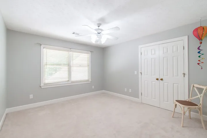 A well-lit bedroom features plush carpeting and a convenient ceiling fan for comfort.