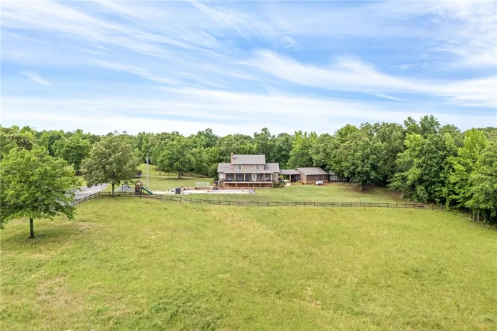 An aerial panorama reveals a private country estate, complete with a main residence, fenced pastures, and an inviting pool.