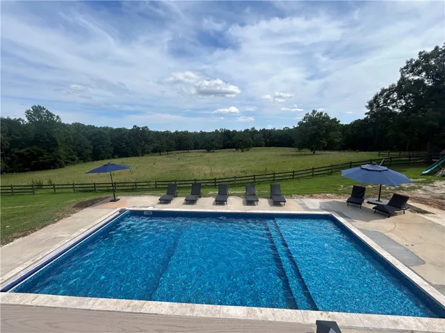 An inviting backyard oasis features a shimmering pool, ample lounging space, and open views of green fields.