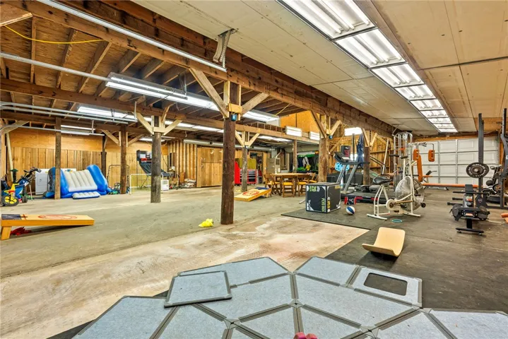 A spacious and adaptable area ideal for recreation or a home gym, featuring exposed wooden beams and durable flooring.