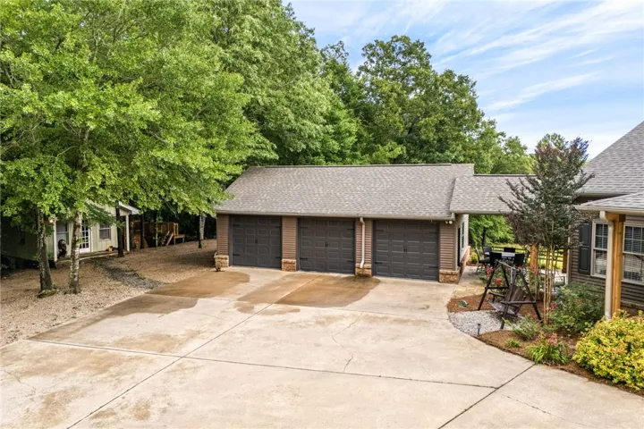 A spacious concrete driveway leads to a triple garage, complemented by mature trees and a charming patio.