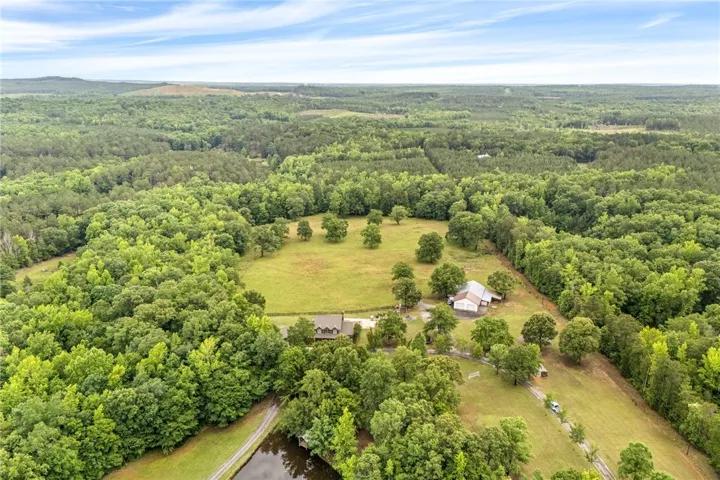 Sprawling estate nestled amidst verdant forests, featuring a serene pond and ample private grounds.